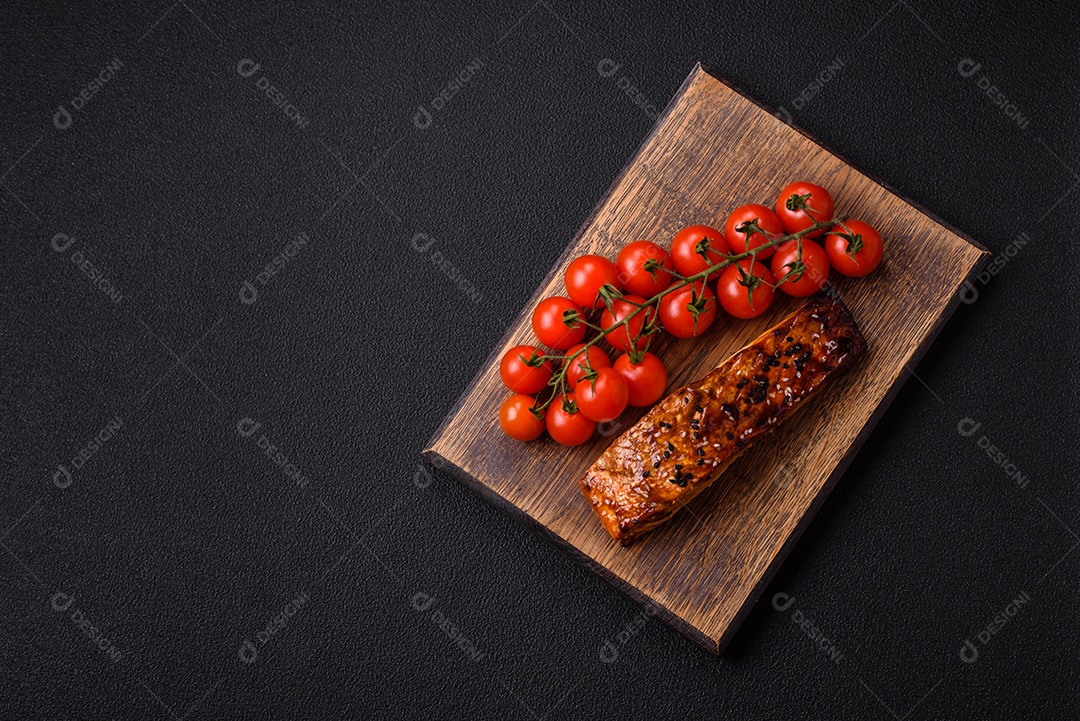 Delicioso salmão vermelho grelhado com molho e gergelim, especiarias e ervas sobre um fundo escuro de concreto