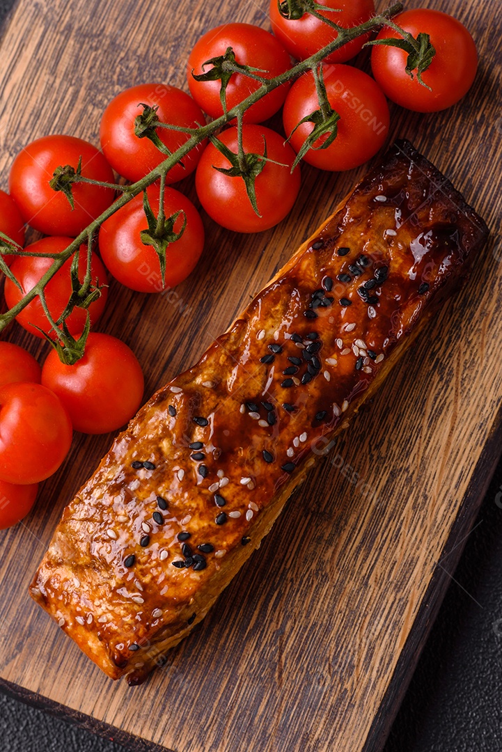 Delicioso salmão vermelho grelhado com molho e gergelim, especiarias e ervas sobre um fundo escuro de concreto