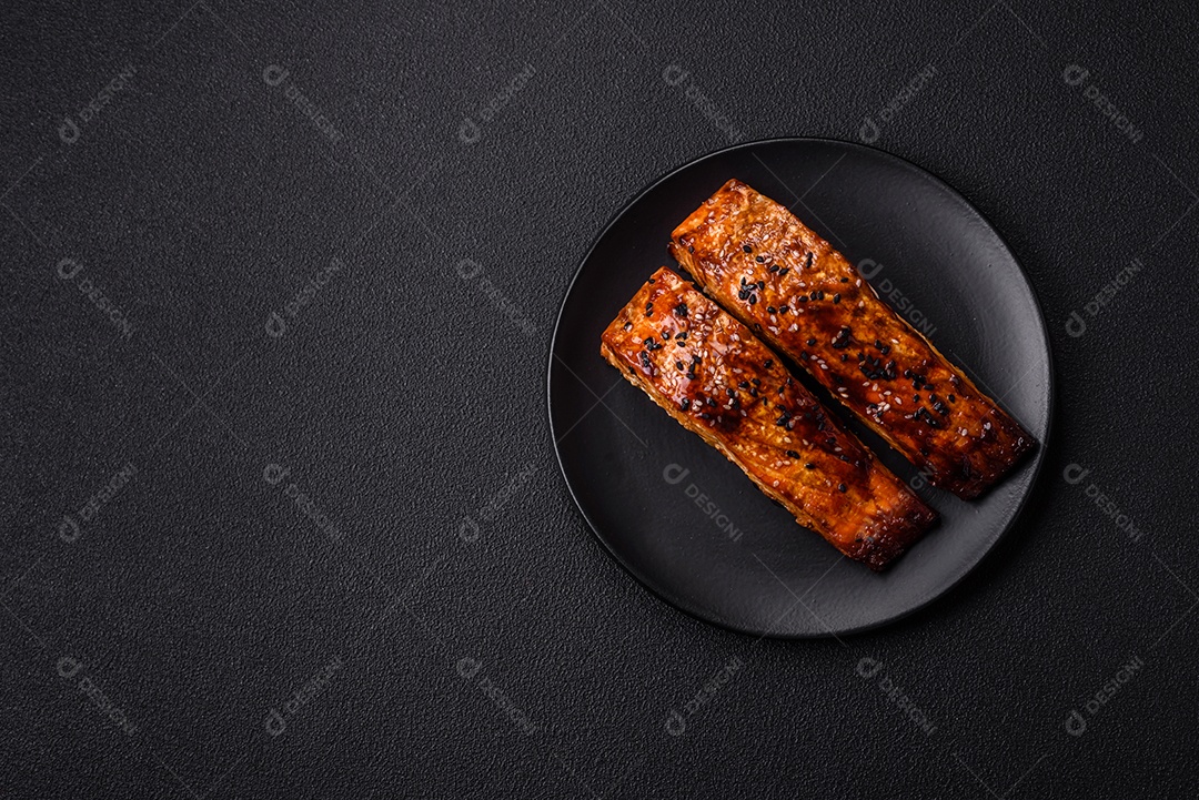 Delicioso salmão vermelho grelhado com molho e gergelim, especiarias e ervas sobre um fundo escuro de concreto