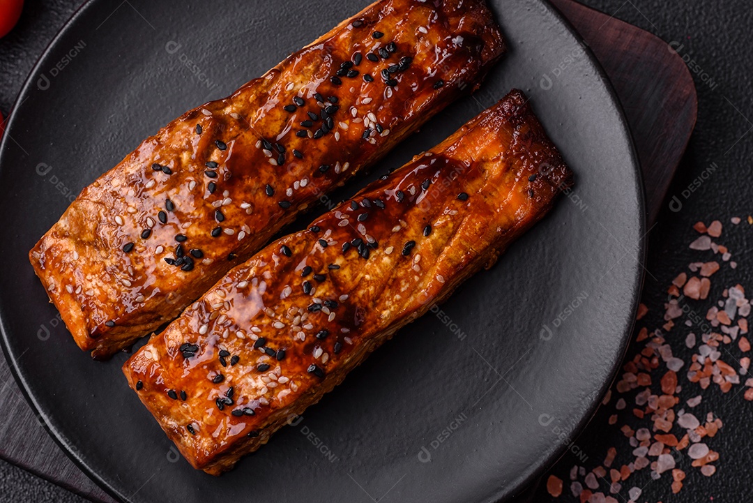 Delicioso salmão vermelho grelhado com molho e gergelim, especiarias e ervas sobre um fundo escuro de concreto