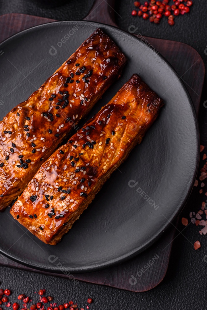 Delicioso salmão vermelho grelhado com molho e gergelim, especiarias e ervas sobre um fundo escuro de concreto
