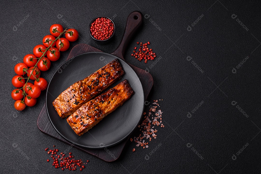Delicioso salmão vermelho grelhado com molho e gergelim, especiarias e ervas sobre um fundo escuro de concreto