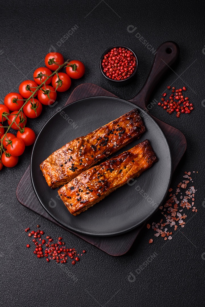 Delicioso salmão vermelho grelhado com molho e gergelim, especiarias e ervas sobre um fundo escuro de concreto