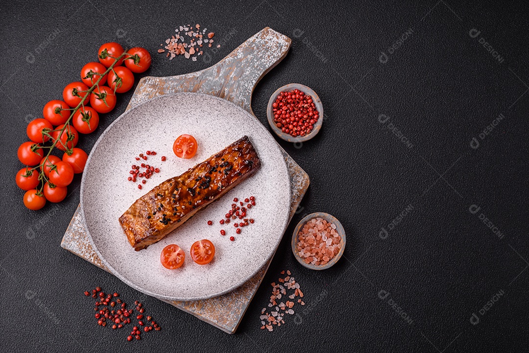 Delicioso salmão vermelho grelhado com molho e gergelim, especiarias e ervas sobre um fundo escuro de concreto