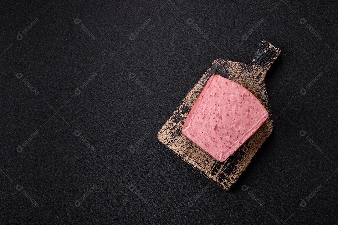 Delicioso presunto rosa enlatado com sal, especiarias e ervas sobre um fundo escuro de concreto