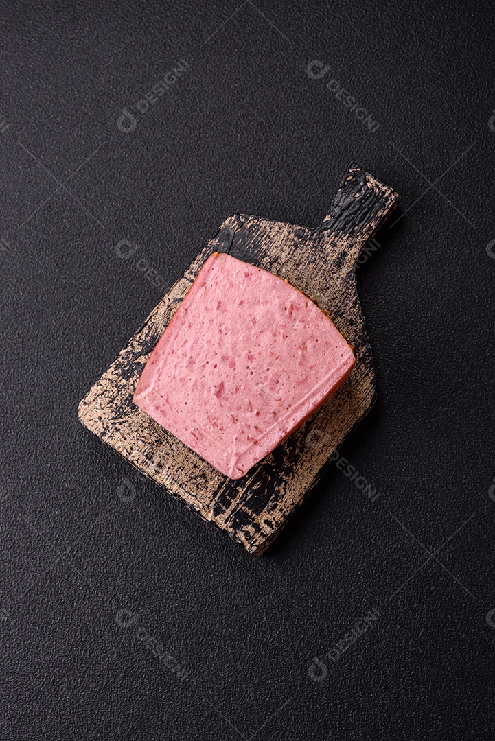 Delicioso presunto rosa enlatado com sal, especiarias e ervas sobre um fundo escuro de concreto