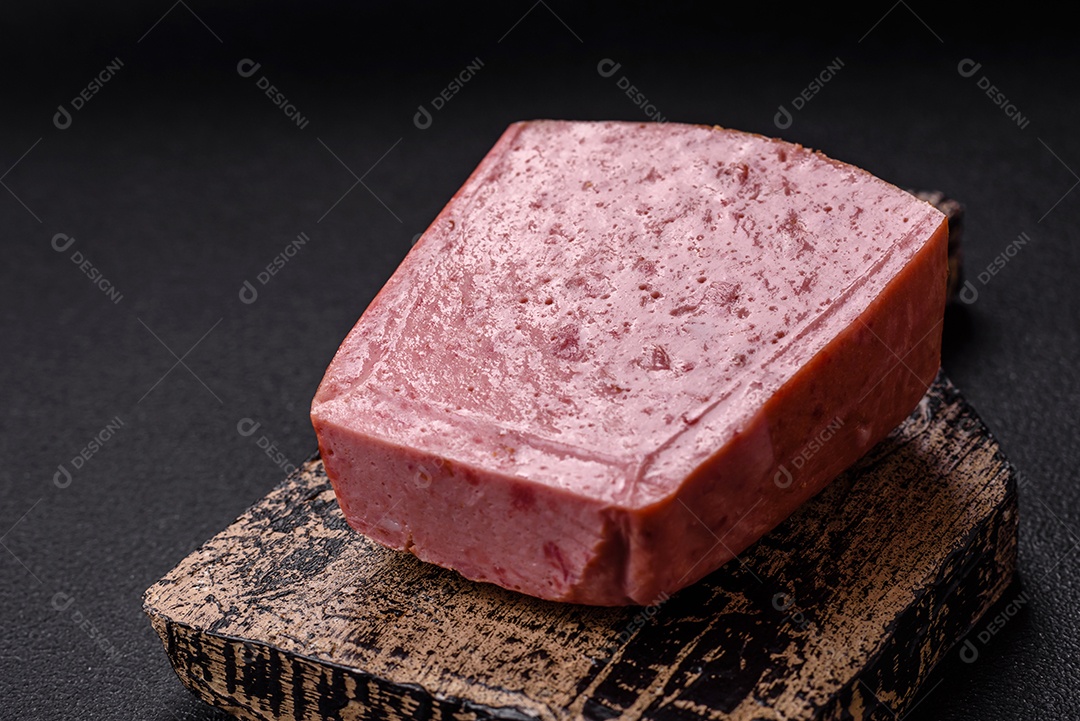 Delicioso presunto rosa enlatado com sal, especiarias e ervas sobre um fundo escuro de concreto