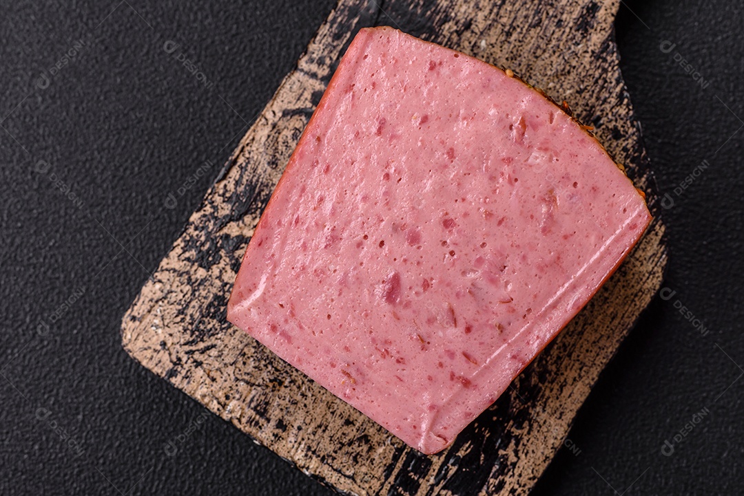 Delicioso presunto rosa enlatado com sal, especiarias e ervas sobre um fundo escuro de concreto