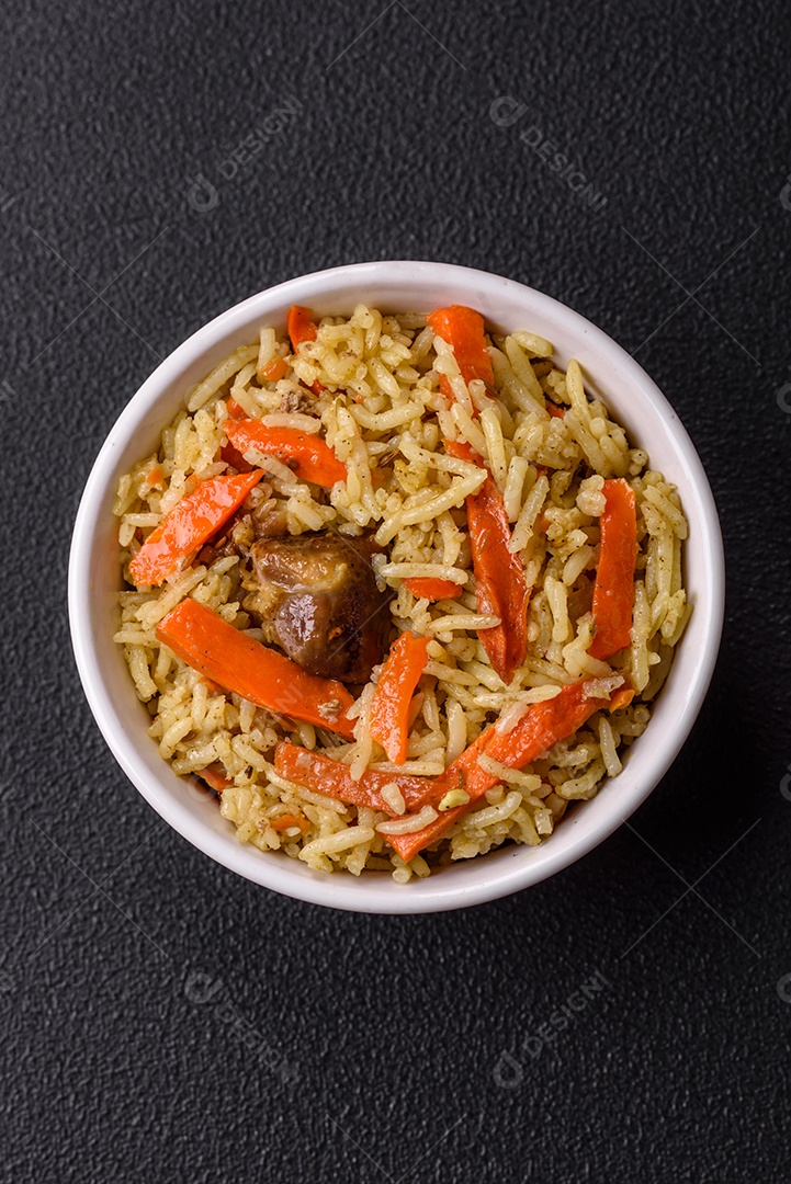 Delicioso pilaf com legumes, sal, especiarias e ervas em uma placa cerâmica sobre um fundo escuro de concreto