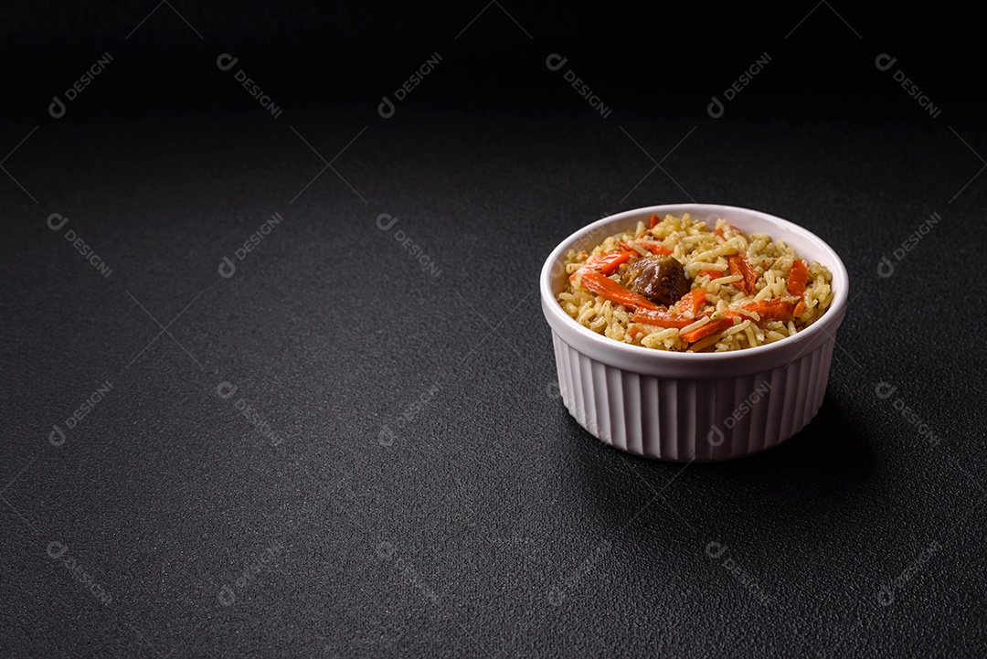 Delicioso pilaf com legumes, sal, especiarias e ervas em uma placa cerâmica sobre um fundo escuro de concreto