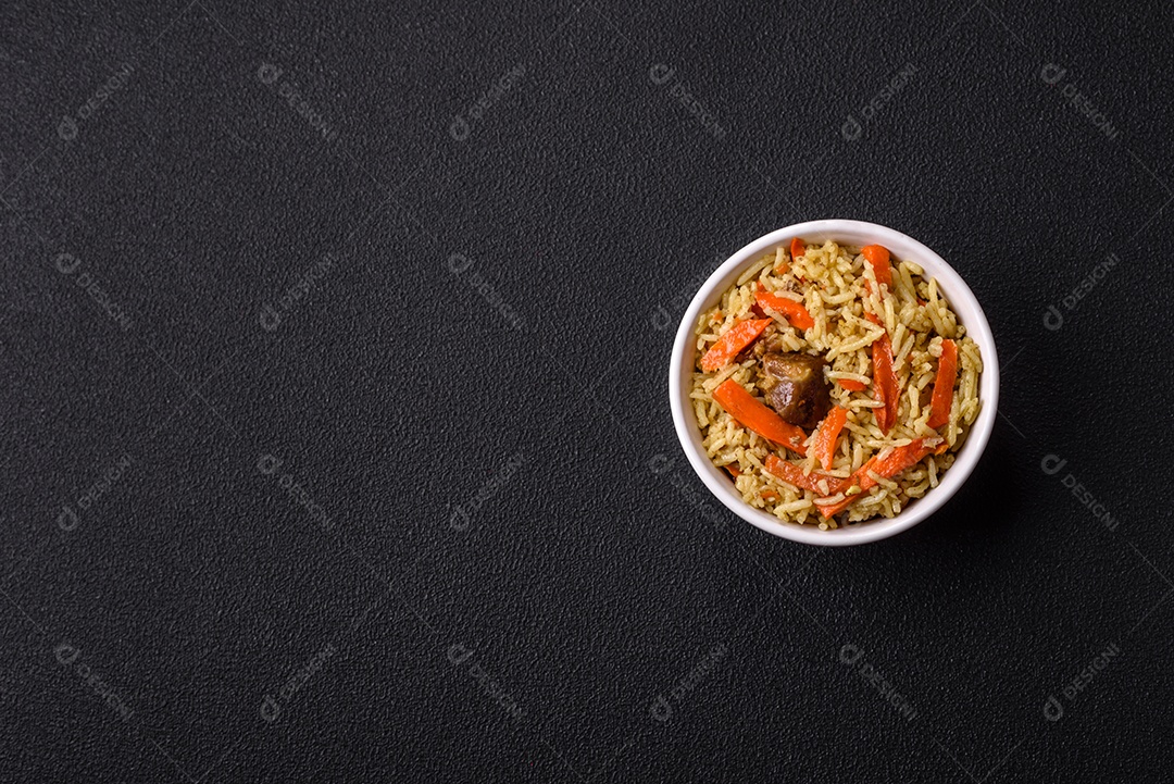 Delicioso pilaf com legumes, sal, especiarias e ervas em uma placa cerâmica sobre um fundo escuro de concreto