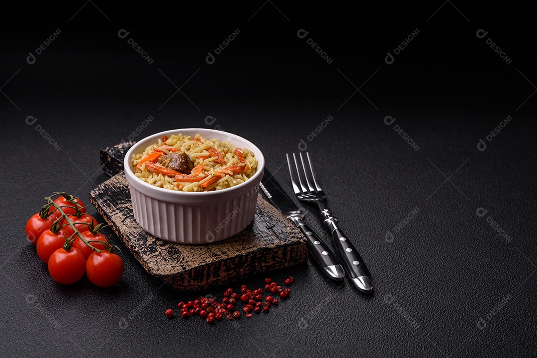 Delicioso pilaf com legumes, sal, especiarias e ervas em uma placa cerâmica sobre um fundo escuro de concreto