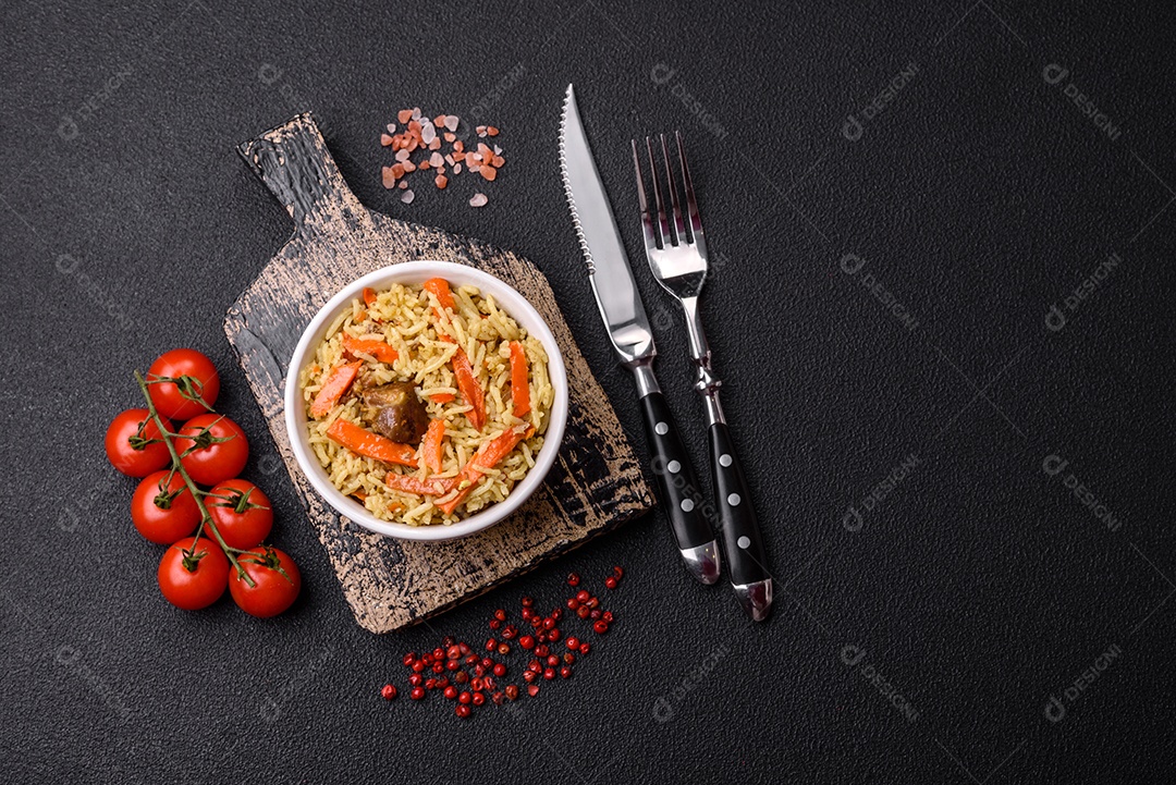 Delicioso pilaf com legumes, sal, especiarias e ervas em uma placa cerâmica sobre um fundo escuro de concreto