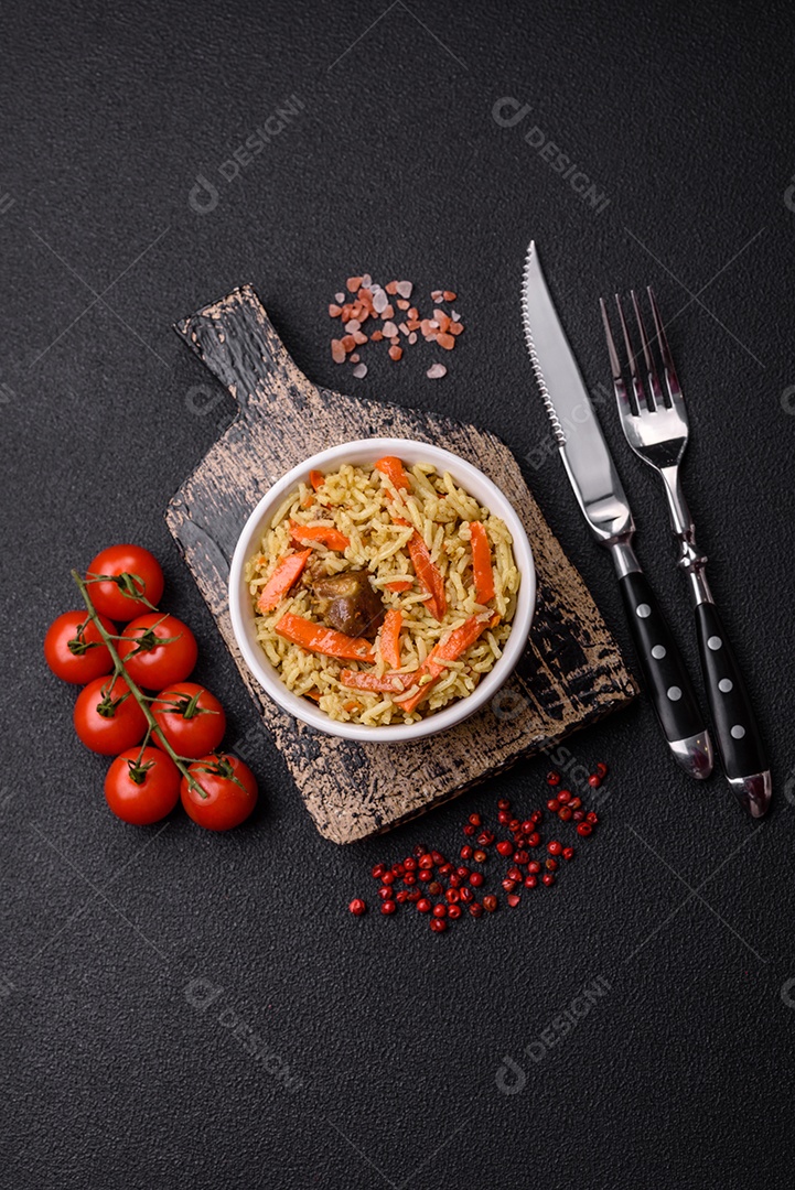 Delicioso pilaf com legumes, sal, especiarias e ervas em uma placa cerâmica sobre um fundo escuro de concreto