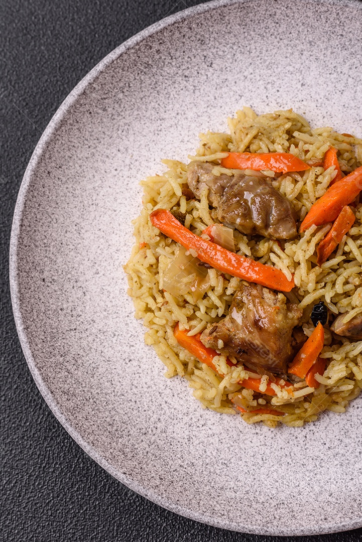 Delicioso pilaf com legumes, sal, especiarias e ervas em uma placa cerâmica sobre um fundo escuro de concreto