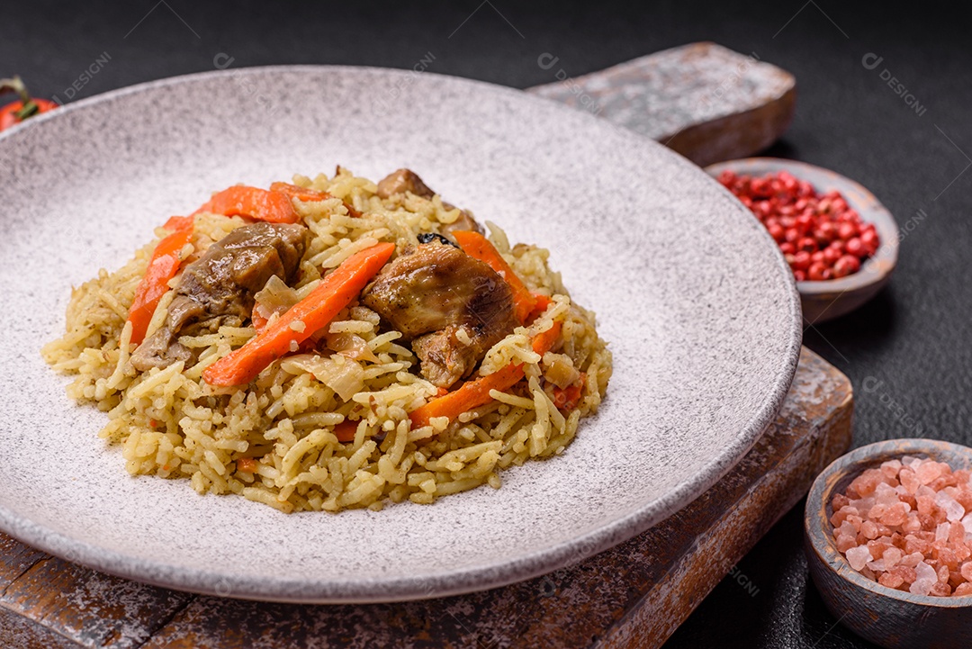 Delicioso pilaf com legumes, sal, especiarias e ervas em uma placa cerâmica sobre um fundo escuro de concreto