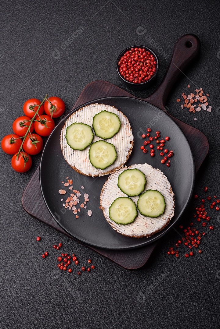 Delicioso sanduíche vegetariano com torradas grelhadas, cream cheese, pepinos e sementes e grãos sobre um fundo escuro de concreto