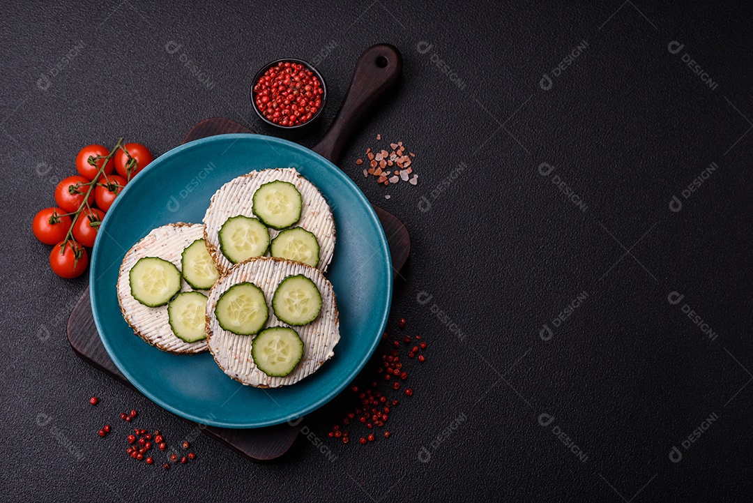 Delicioso sanduíche vegetariano com torradas grelhadas, cream cheese, pepinos e sementes e grãos sobre um fundo escuro de concreto