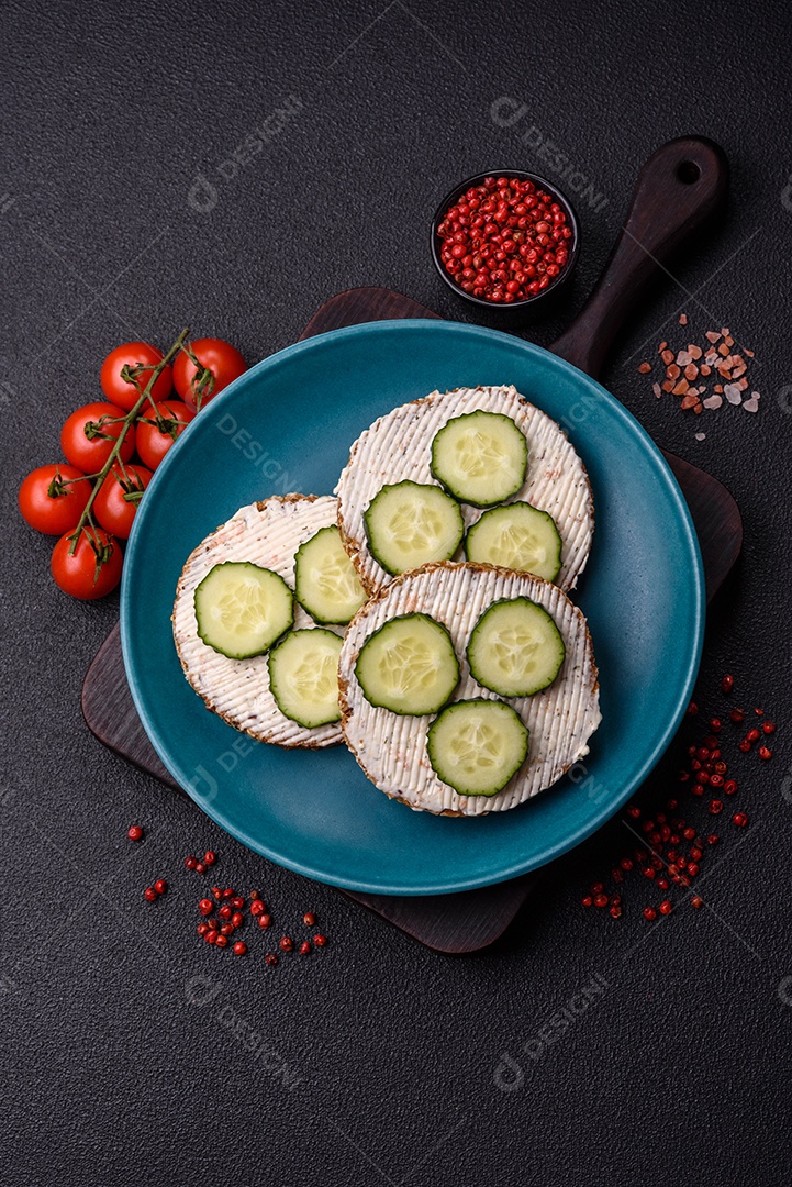 Delicioso sanduíche vegetariano com torradas grelhadas, cream cheese, pepinos e sementes e grãos sobre um fundo escuro de concreto