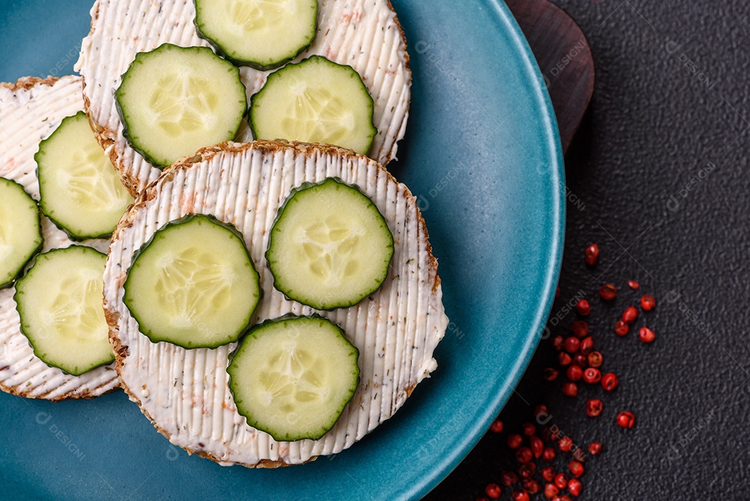 Delicioso sanduíche vegetariano com torradas grelhadas, cream cheese, pepinos e sementes e grãos sobre um fundo escuro de concreto