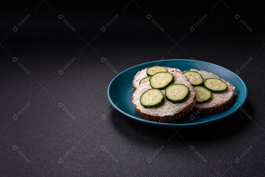 Delicioso sanduíche vegetariano com torradas grelhadas, cream cheese, pepinos e sementes e grãos sobre um fundo escuro de concret