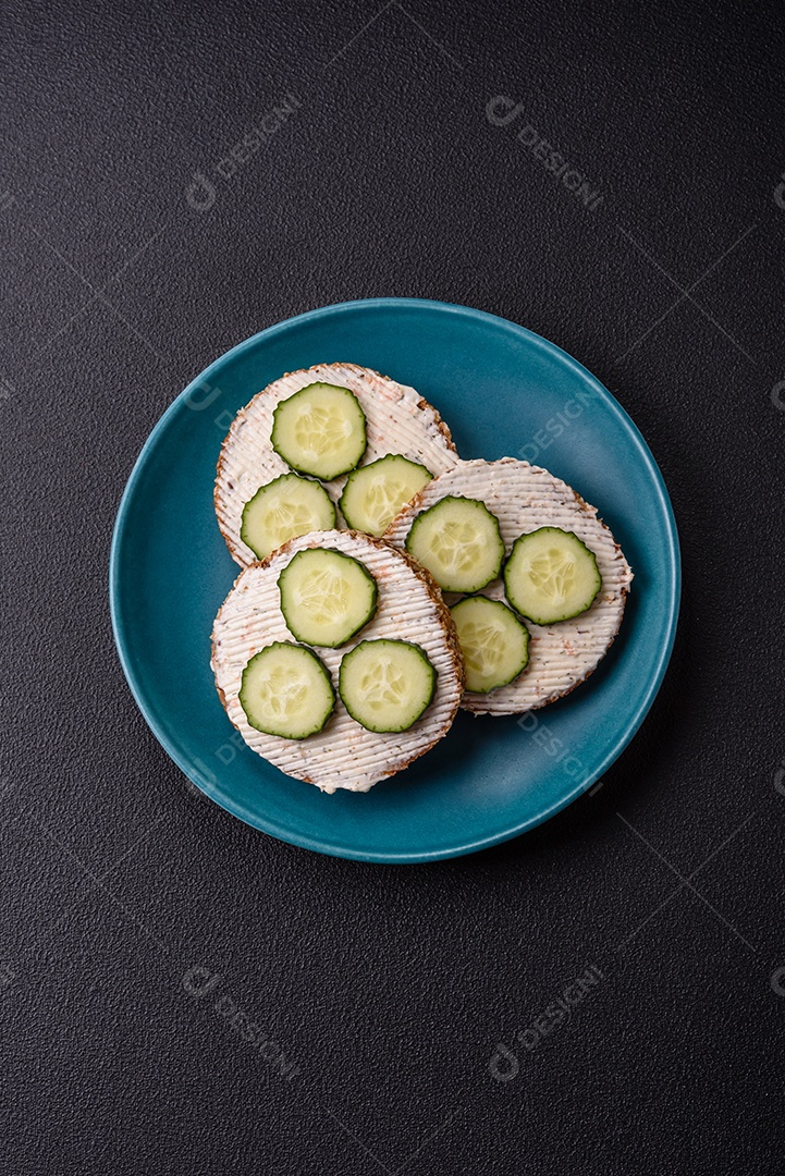 Delicioso sanduíche vegetariano com torradas grelhadas, cream cheese, pepinos e sementes e grãos sobre um fundo escuro de concreto