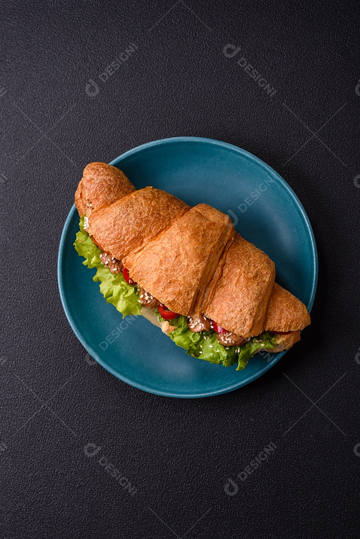 Delicioso croissant crocante fresco com frango ou carne bovina, alface, tomate, especiarias e molho sobre um fundo escuro de concreto