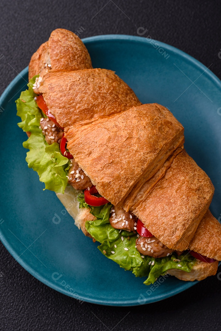 Delicioso croissant crocante fresco com frango ou carne bovina, alface, tomate, especiarias e molho sobre um fundo escuro de concreto