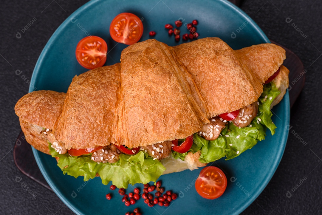 Delicioso croissant crocante fresco com frango ou carne bovina, alface, tomate, especiarias e molho sobre um fundo escuro de concreto