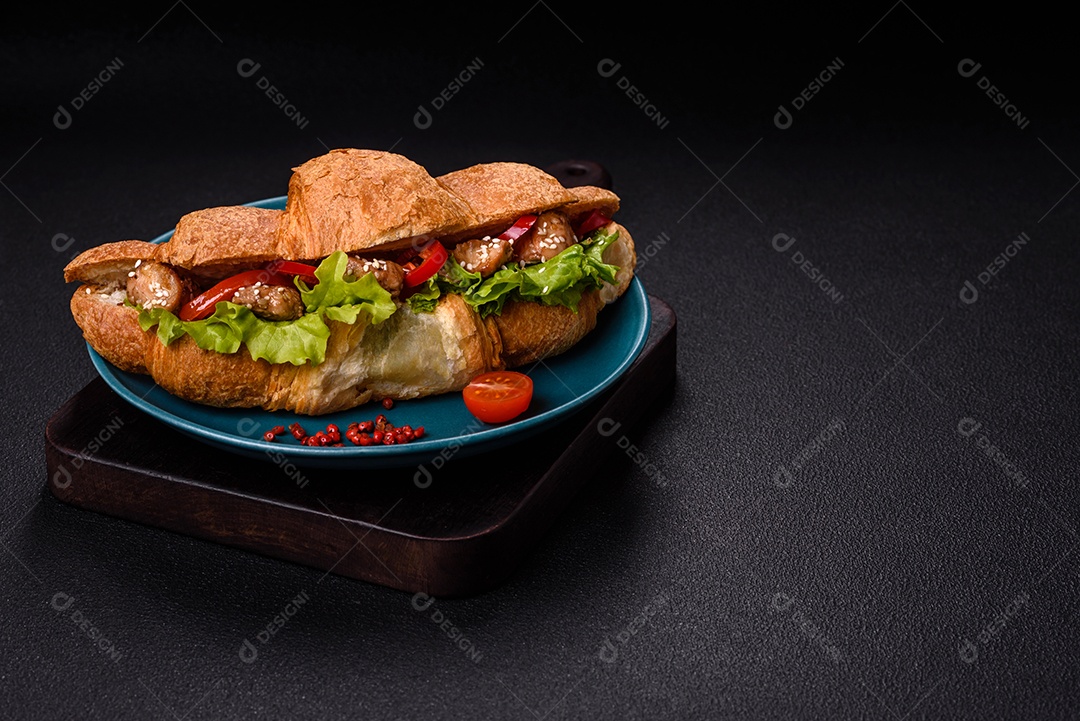 Delicioso croissant crocante fresco com frango ou carne bovina, alface, tomate, especiarias e molho sobre um fundo escuro de concreto
