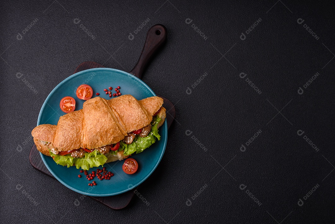 Delicioso croissant crocante fresco com frango ou carne bovina, alface, tomate, especiarias e molho sobre um fundo escuro de concreto