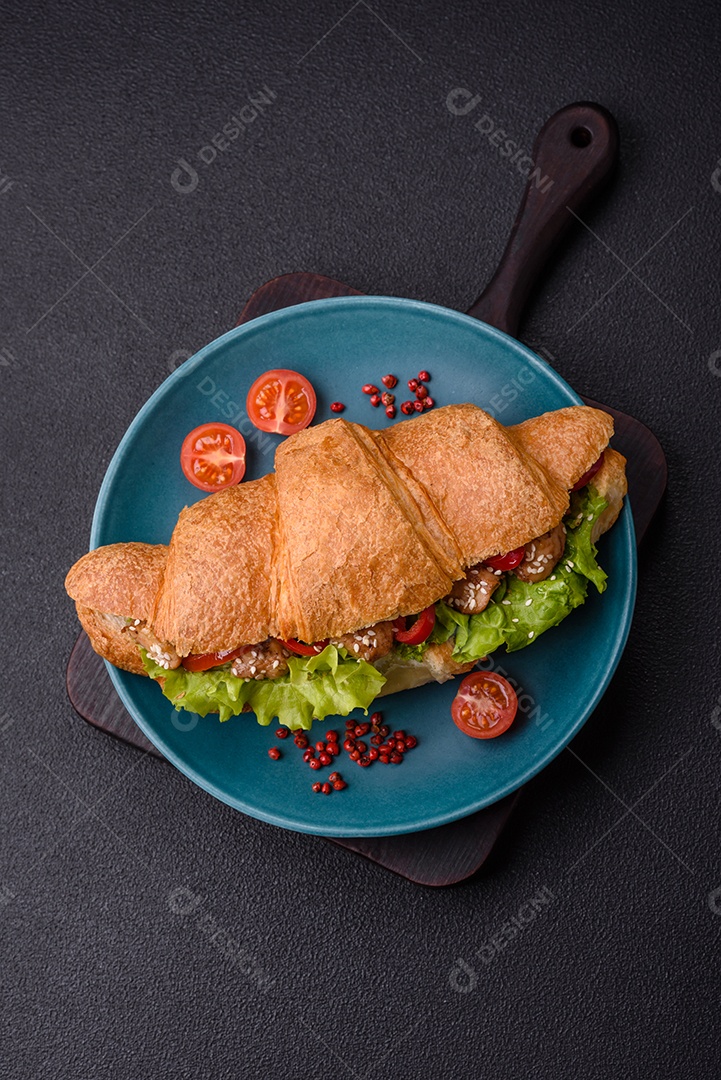 Delicioso croissant crocante fresco com frango ou carne bovina, alface, tomate, especiarias e molho sobre um fundo escuro de concreto