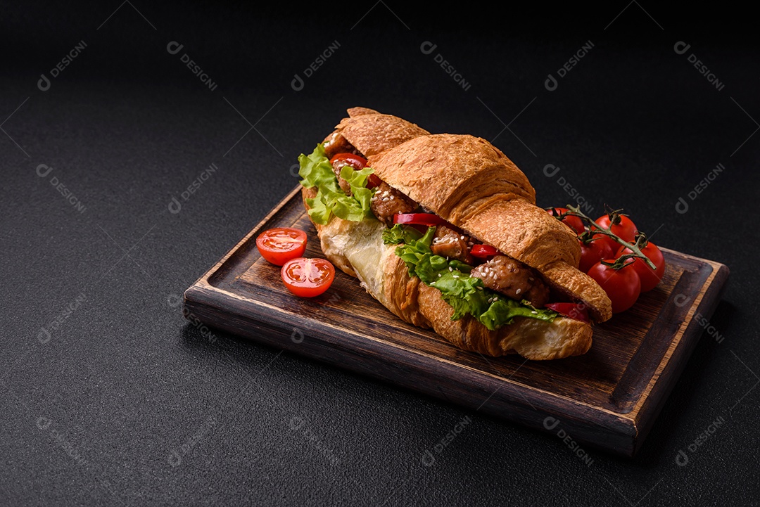 Delicioso croissant crocante fresco com frango ou carne bovina, alface, tomate, especiarias e molho sobre um fundo escuro de concreto