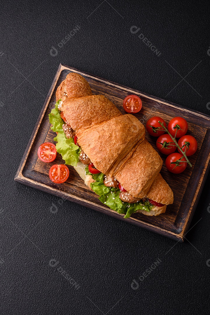 Delicioso croissant crocante fresco com frango ou carne bovina, alface, tomate, especiarias e molho sobre um fundo escuro de concret