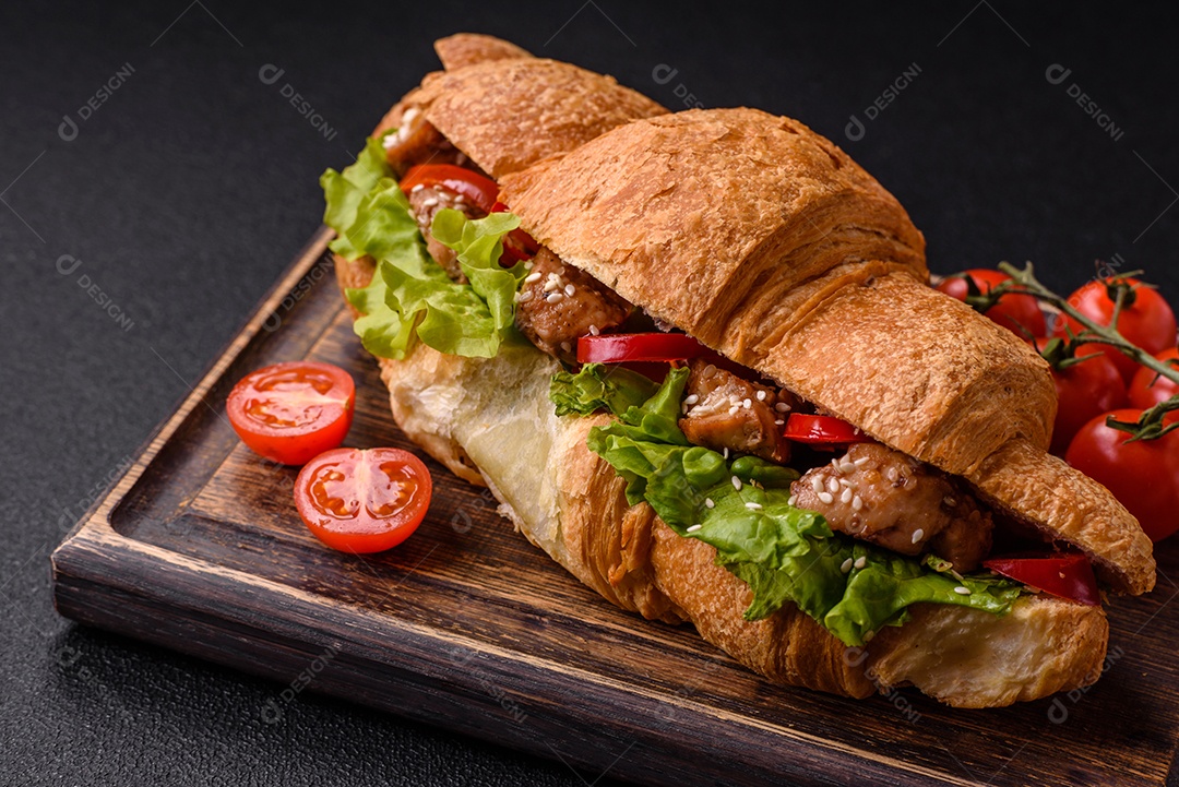 Delicioso croissant crocante fresco com frango ou carne bovina, alface, tomate, especiarias e molho sobre um fundo escuro de concreto