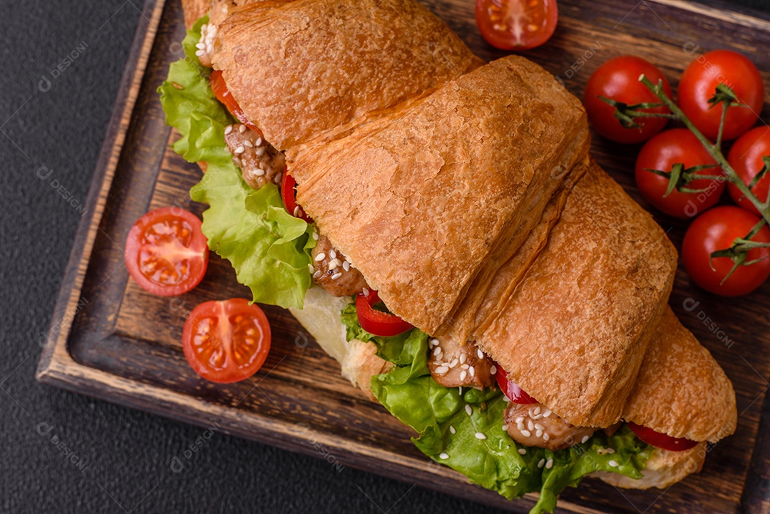 Delicioso croissant crocante fresco com frango ou carne bovina, alface, tomate, especiarias e molho sobre um fundo escuro de concreto