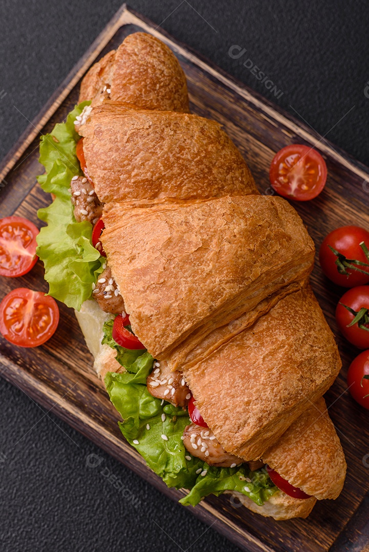 Delicioso croissant crocante fresco com frango ou carne bovina, alface, tomate, especiarias e molho sobre um fundo escuro de concreto