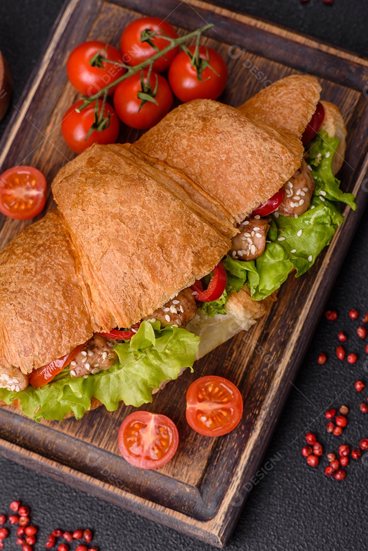 Delicioso croissant crocante fresco com frango ou carne bovina, alface, tomate, especiarias e molho sobre um fundo escuro de concreto