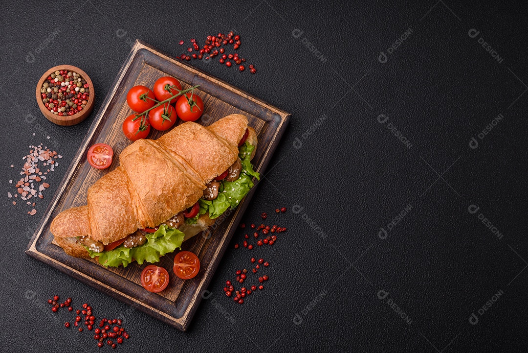 Delicioso croissant crocante fresco com frango ou carne bovina, alface, tomate, especiarias e molho sobre um fundo escuro de concreto