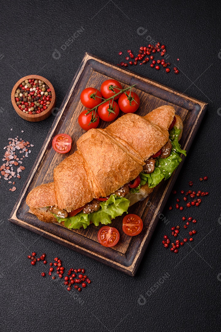 Delicioso croissant crocante fresco com frango ou carne bovina, alface, tomate, especiarias e molho sobre um fundo escuro de concreto