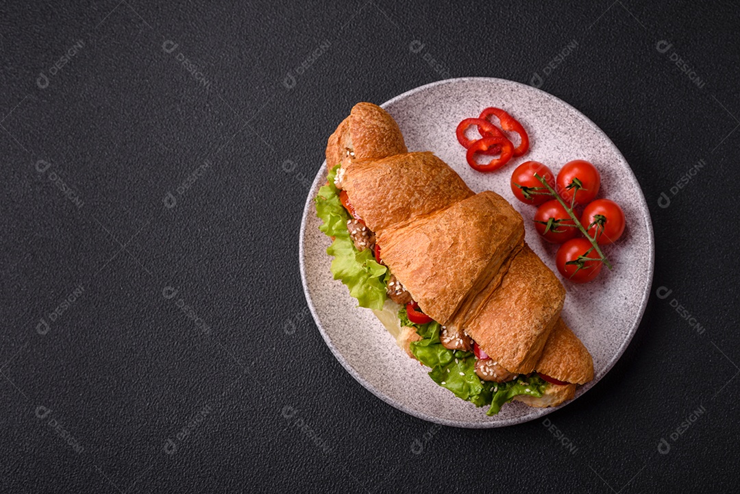 Delicioso croissant crocante fresco com frango ou carne bovina, alface, tomate, especiarias e molho sobre um fundo escuro de concreto