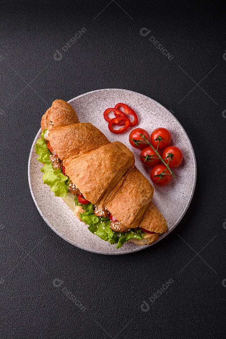 Delicioso croissant crocante fresco com frango ou carne bovina, alface, tomate, especiarias e molho sobre um fundo escuro de concreto
