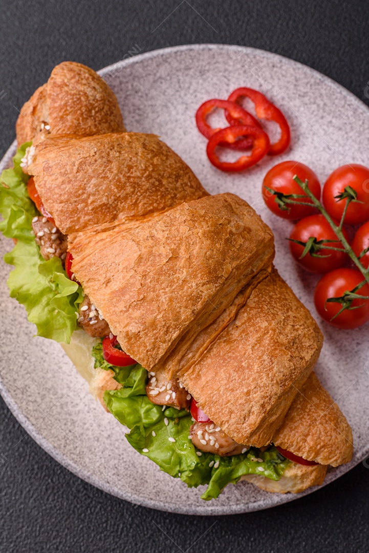 Delicioso croissant crocante fresco com frango ou carne bovina, alface, tomate, especiarias e molho sobre um fundo escuro de concreto