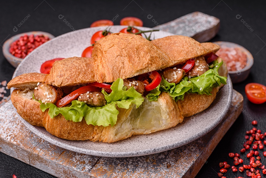 Delicioso croissant crocante fresco com frango ou carne bovina, alface, tomate, especiarias e molho sobre um fundo escuro de concreto