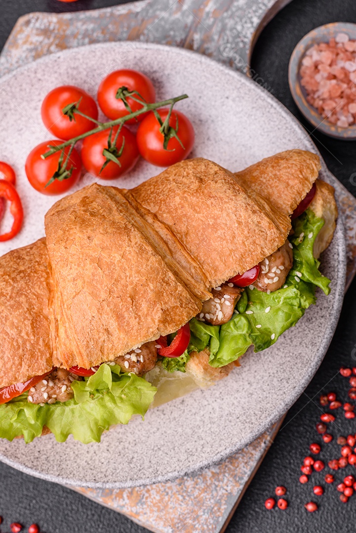 Delicioso croissant crocante fresco com frango ou carne bovina, alface, tomate, especiarias e molho sobre um fundo escuro de concreto