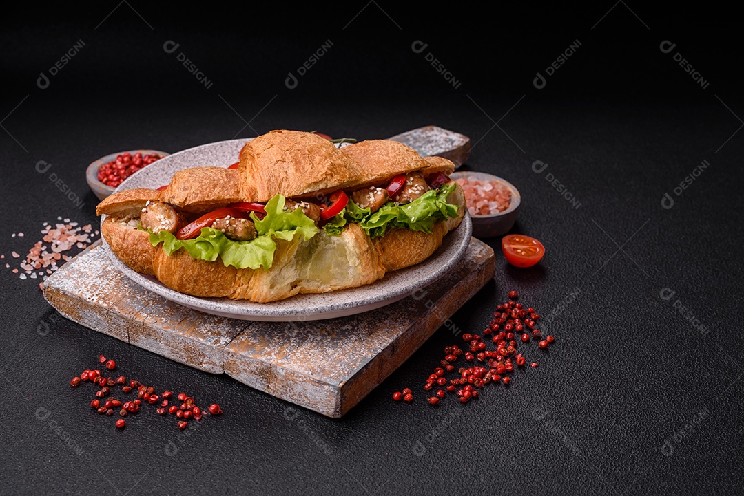 Delicioso croissant crocante fresco com frango ou carne bovina, alface, tomate, especiarias e molho sobre um fundo escuro de concreto