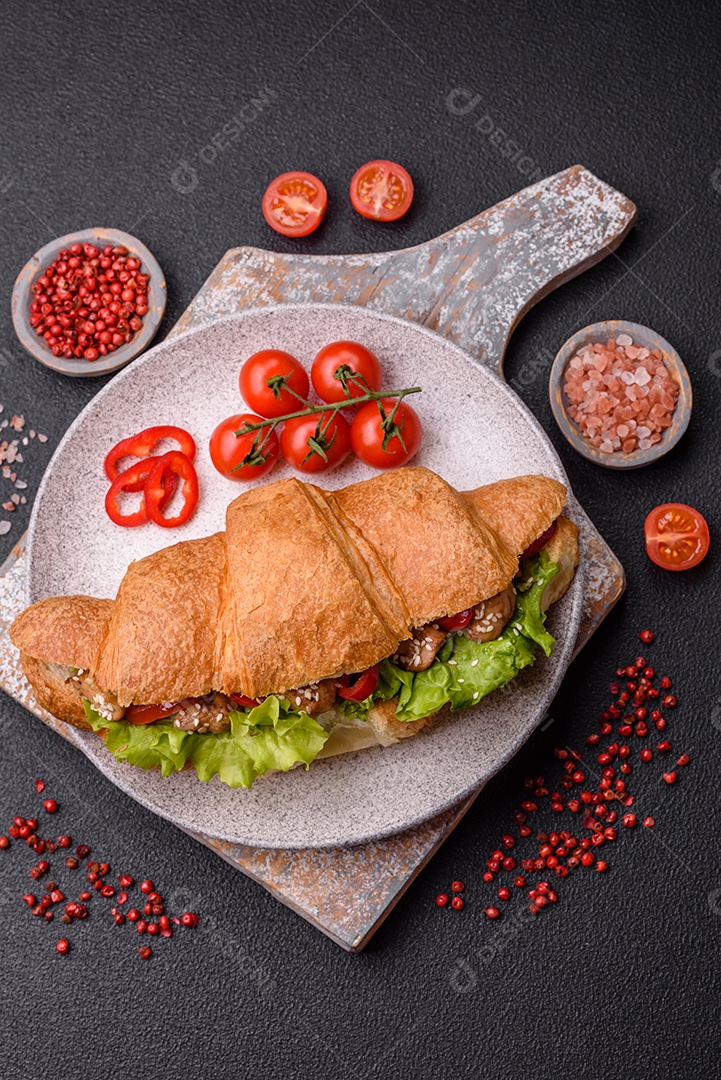 Delicioso croissant crocante fresco com frango ou carne bovina, alface, tomate, especiarias e molho sobre um fundo escuro de concreto