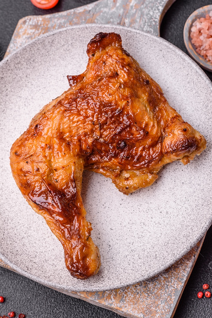 Deliciosa coxa ou quarto de frango grelhado com sal e especiarias em fundo escuro de concreto