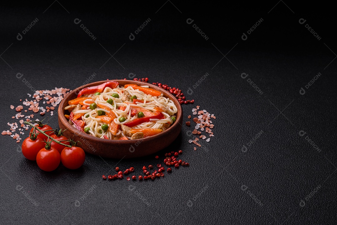 Delicioso macarrão de arroz ou udon com frango, cenoura, pimenta, sal, especiarias e ervas sobre fundo escuro de concreto