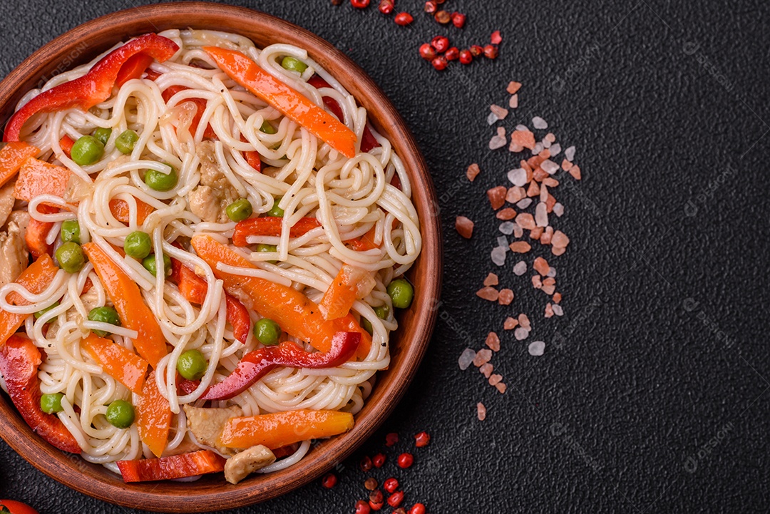 Delicioso macarrão de arroz ou udon com frango, cenoura, pimenta, sal, especiarias e ervas sobre fundo escuro de concreto